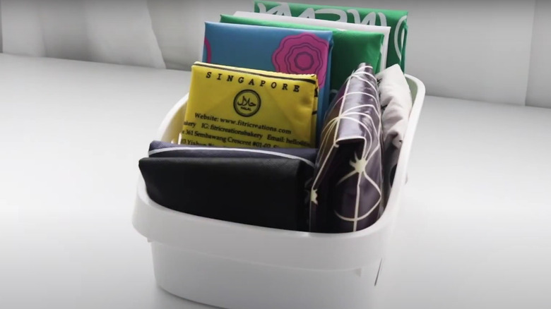 A small white plastic bin of reusable bags all folded into small square bundles
