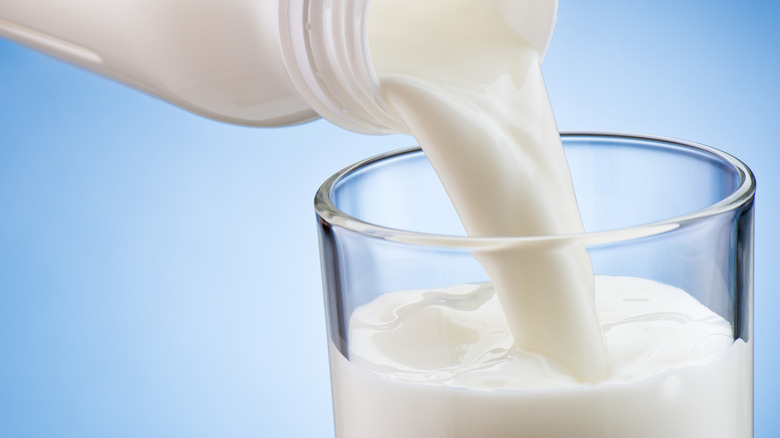 Milk pouring in a glass from a bottle on a blue background