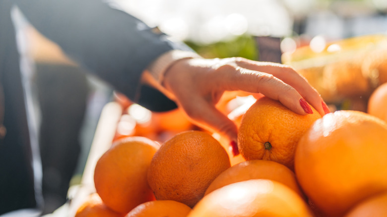 Hand picking out oranges at a market in the sun.
