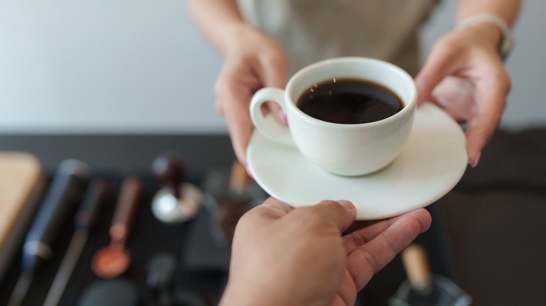 barista hands over a cup of black coffee