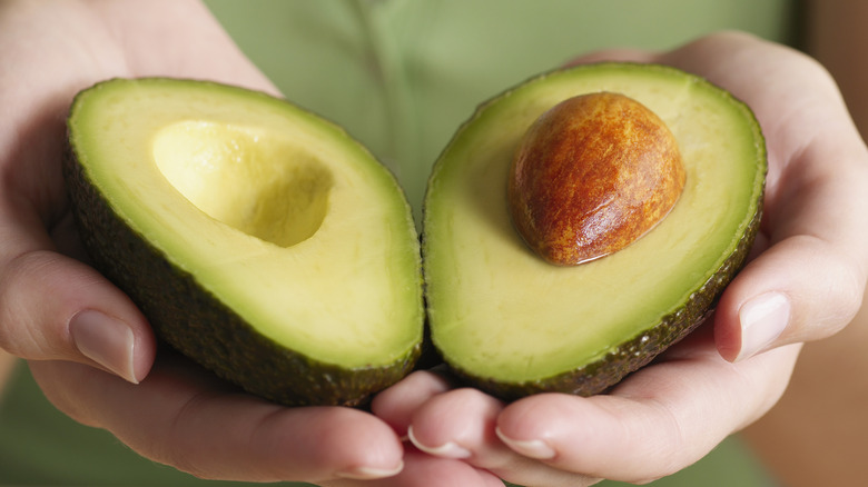 Woman holding two halves of a cut avocado