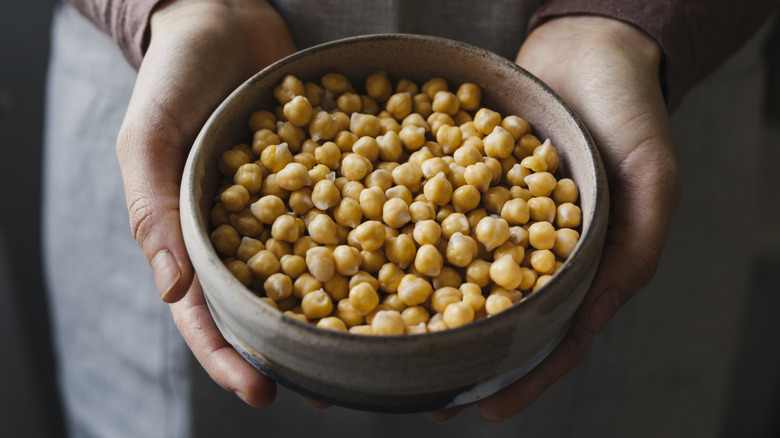 Someone holding chickpeas in a clay bowl