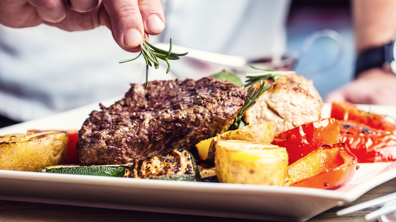 A chef adds rosemary to a dish