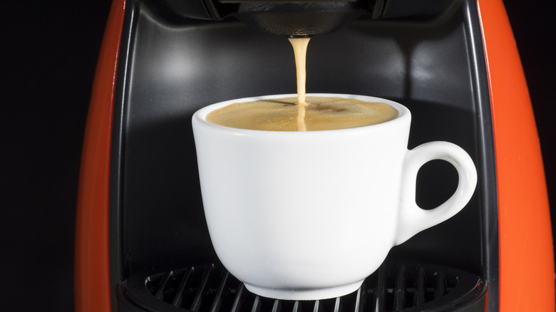 Close-up of coffee pouring from a black and red machine into a white cup