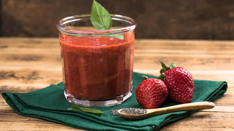 strawberry smoothie in glass next to wooden spoon with chia seeds, two fresh strawberries