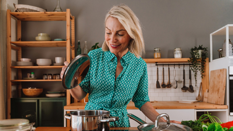 Woman lifts the lid on a pot cooking in the stove