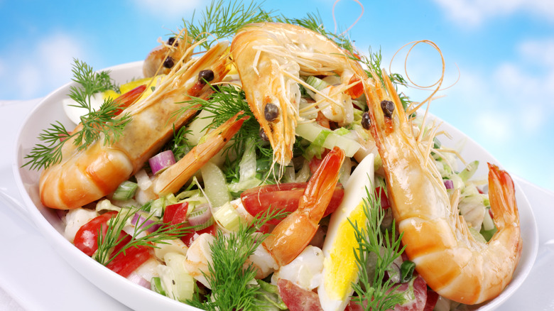 Bowl of Shrimp Louie salad with large shrimp, hard boiled eggs, tomatoes, red onion, and dill