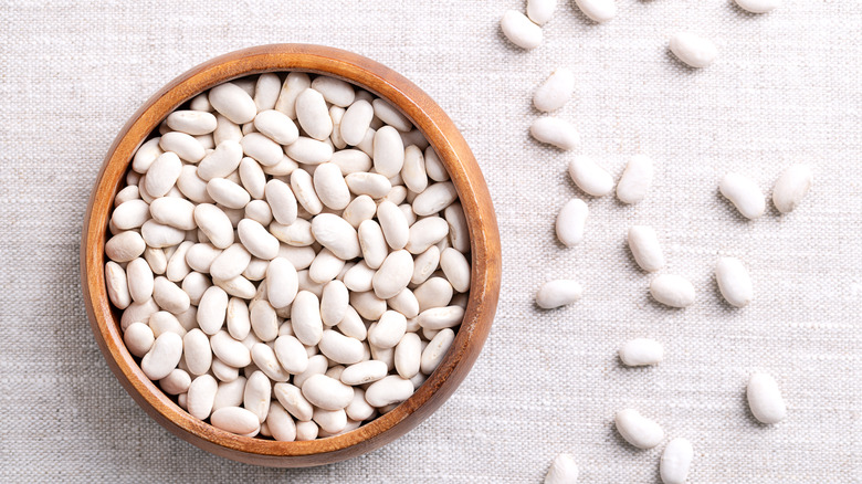 A small wooden bowl filled with white beans on a cloth background