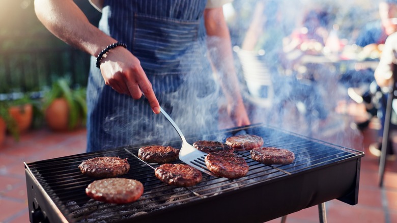 home cook in apron flips grilled burgers