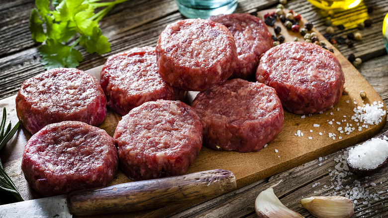 Raw hamburger patties on a wooden cutting board