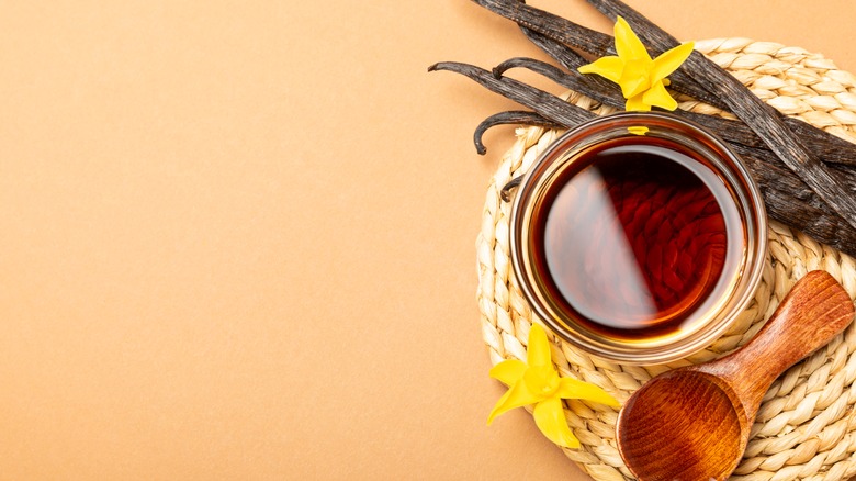Overhead view of vanilla extract in ramekin with wood spoon and vanilla pods.