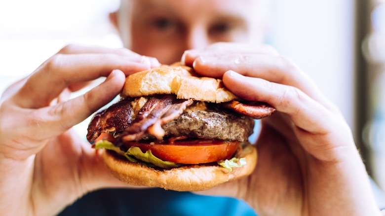 man holds up hefty bacon burger