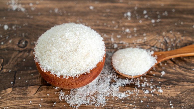 A close-up of an overflowing wooden bowl and spoon of sugar
