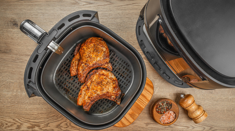 A top-down shot of an air fryer with its basket removed and two browned steaks inside