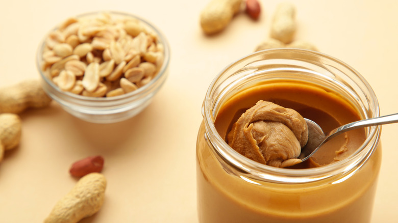 Jar of peanut butter with spoon and bowl of peanuts in background