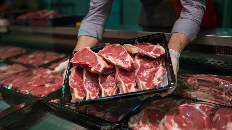 hands hold trays of steaks in a butcher case