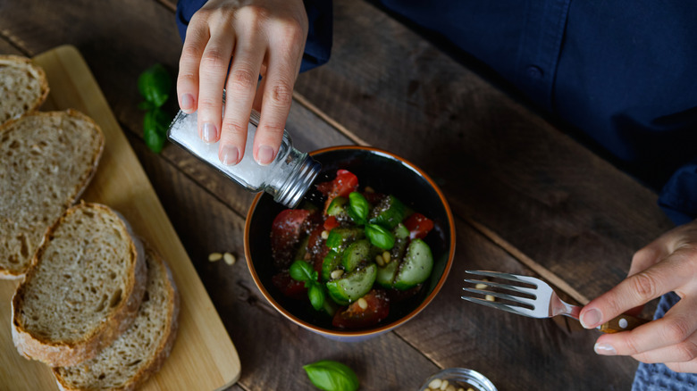 Adding salt to a salad with a salt shaker.