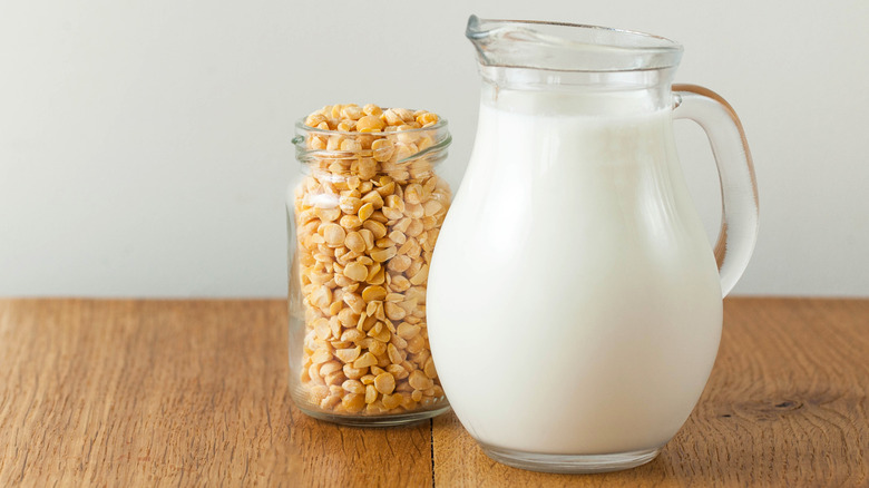 Vegetable pea milk in a jug and peas in a jar on a wooden table against a pale beige background
