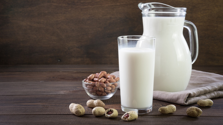 Fresh peanut milk in glass and pitcher on dark wooden table.