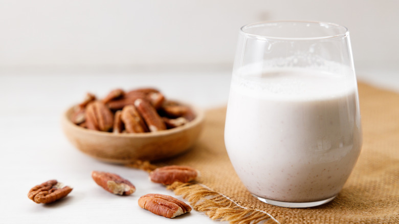 Pecan milk in a glass with raw pecan nuts on wooden table