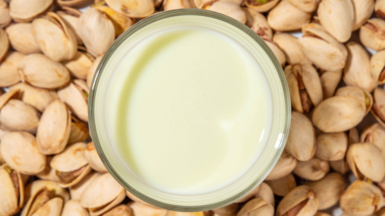 A top-down vewi of a glass of pistachio milk surrounded by pistachio nuts