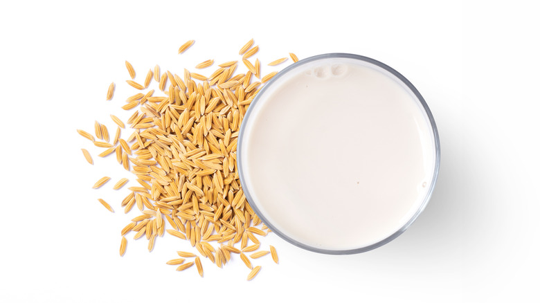 Top-down view of a glass of rice milk next to a pile of rice grains on a white background