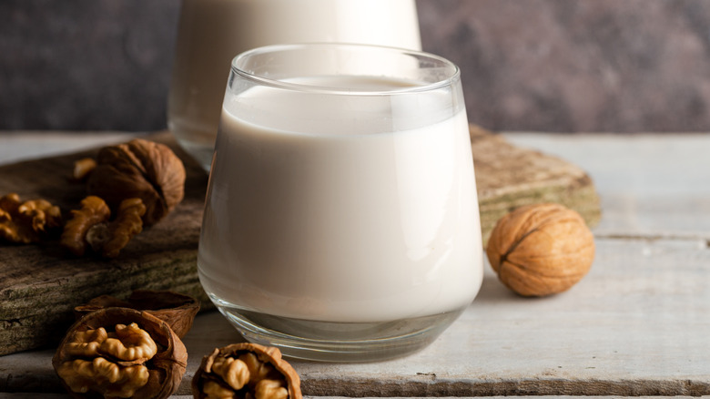 Close-up of two glasses of walnut milk, next to open and closed walnuts, on wooden table