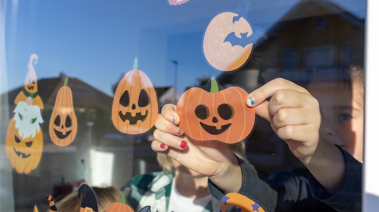 child's hands place pumpkin window clings