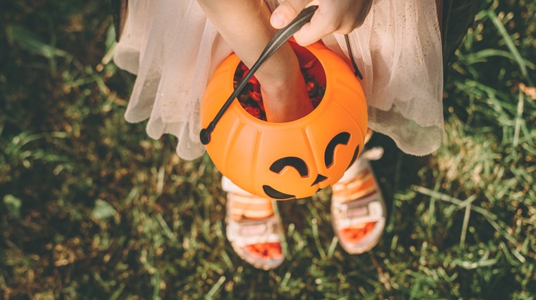 hand reaches into a trick-or-treat pumpkin bucket