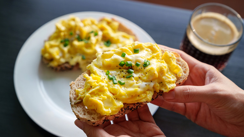 hands hold bread with creamy scrambled egg on top