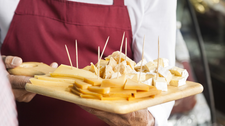 man in an apron holding a wood serving platter with cheese samples