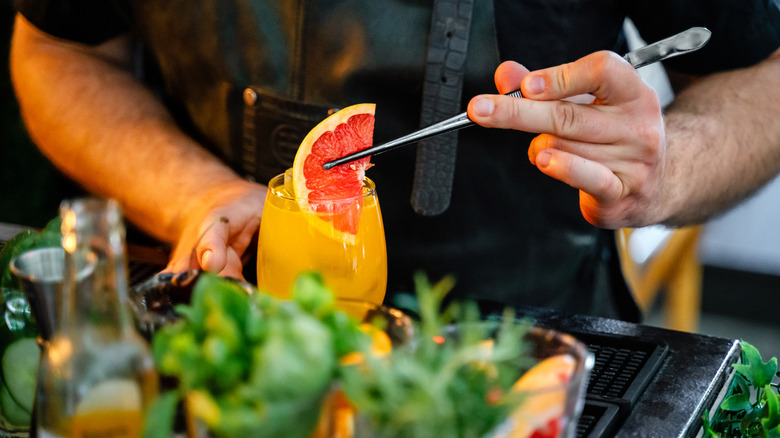 Bartender adds an orange wedge to a cocktail