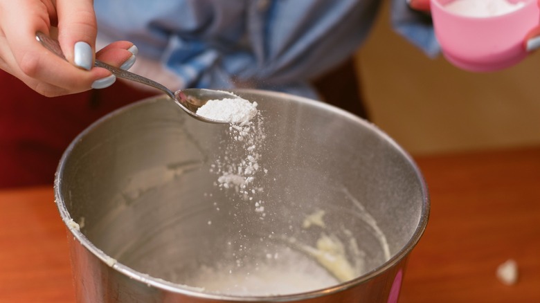 Person adding baking soda to cake batter in bowl