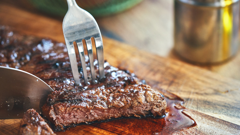 cooked-through steak being sliced with knife and fork