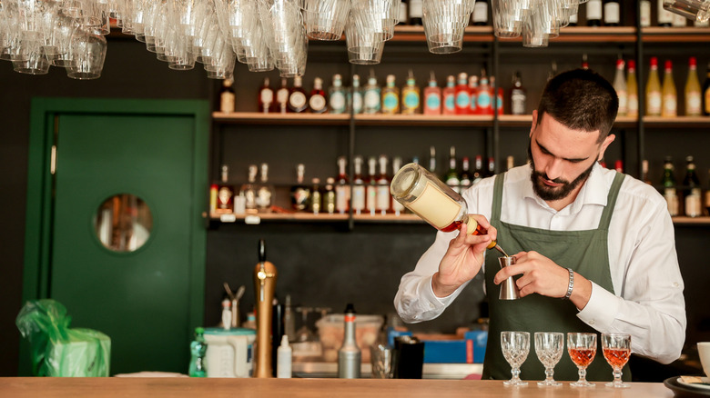 Male bartender with beard measuring shots at upscale looking bar.