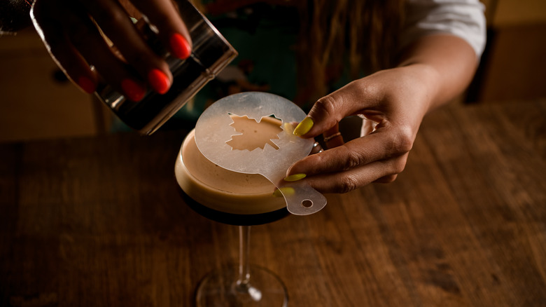 Pouring cocoa powder through a stencil on a drink
