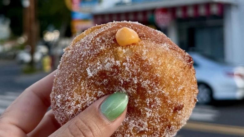 Hand holding a small sugared donut with pumpkin spice filling outside