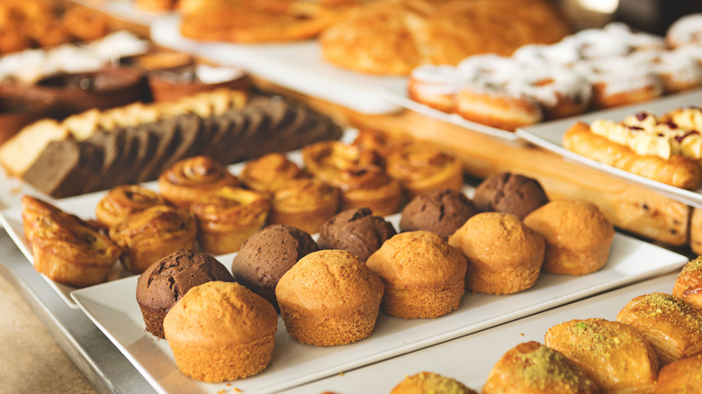 Close-up variety of freshly baked pastries, muffins and sweet rolls displayed on buffet table in cozy bakery or cafe setting