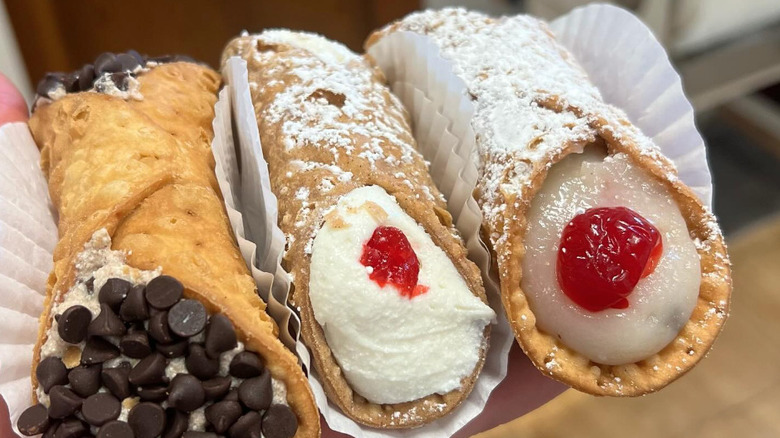Lineup of three stuffed cannolis in paper wrappers