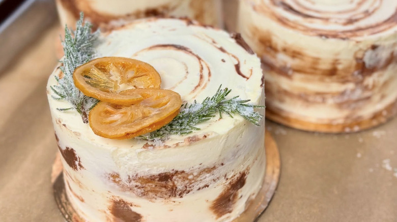 Three layered cakes with a crumb coat of frosting, candied citrus, and sugared rosemary