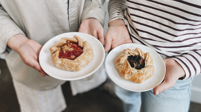 Two people each holding a plate with a fruit galette or Danish