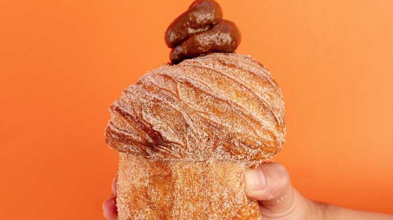 Hand holding a filled cruffin in front of an orange wall