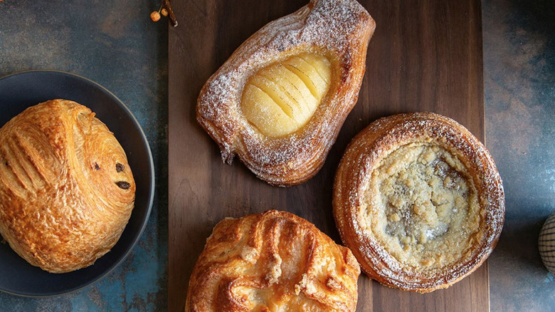 Overhead image with dark wood serving tray with a tart, croissant, and two other pastries