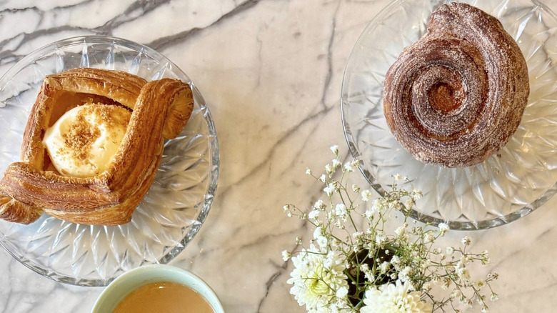 Overhead image of marble table with two glass plates with a croissant and cinnamon roll