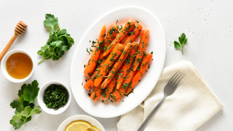 plate of honey glazed carrots with fresh herbs, surrounded by ingredients.