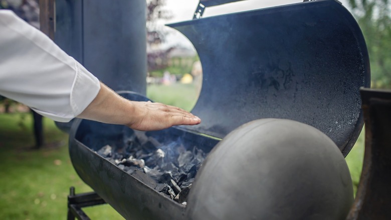 a hand feels the heat coming off a smoker