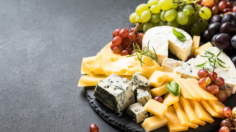 Different types of cheeses on platter with grapes