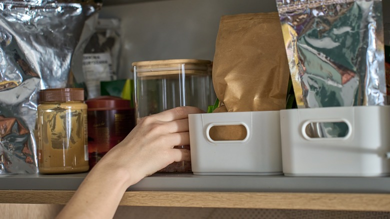 Hand reaches for container on cluttered kitchen shelf