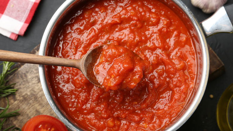 A close-up of a bowl of tomato sauce being stirred by a wooden spoon