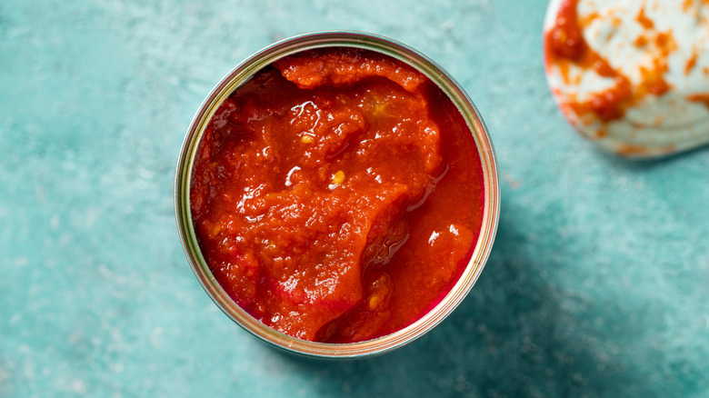 Opened can of tomato sauce on blue counter, overhead shot.